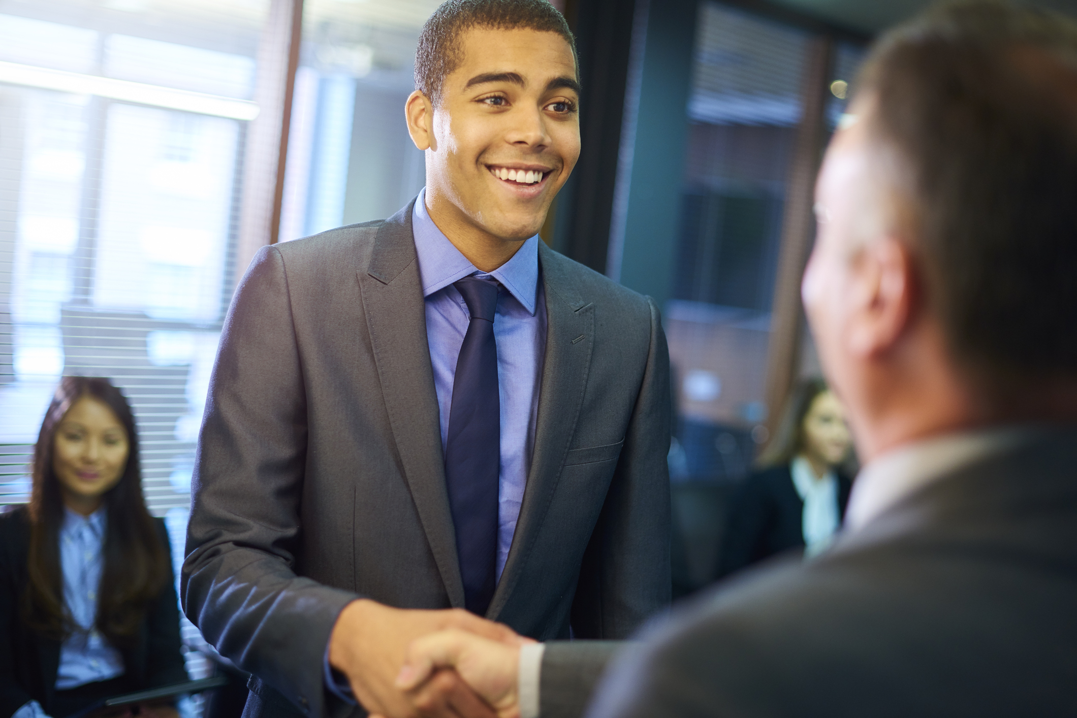 young man steps forward as he is called in for his interview and shakes hands with his possible new employer.