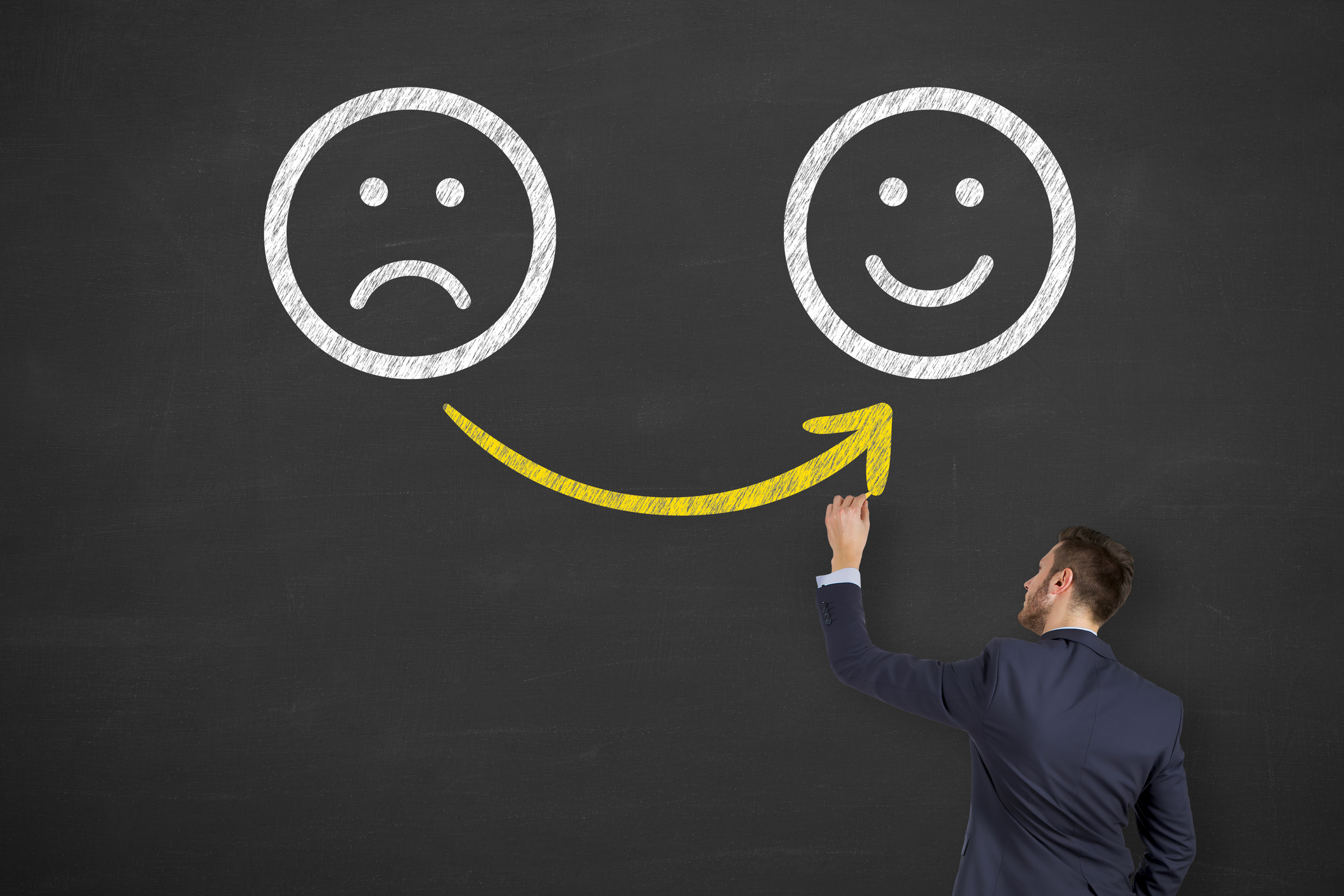 A man drawing happy and unhappy faces on a blackboard.